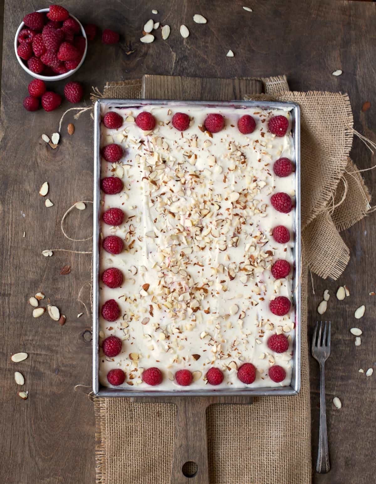 White Raspberry Poke Cake in a silver pan next to a bowl of raspberries