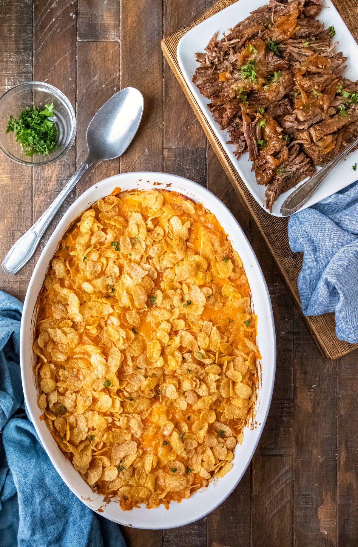 White baking dish with funeral potatoes next to a plate of meat