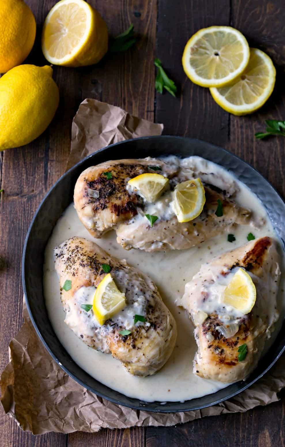 Creamy Crock Pot Lemon Chicken in sauce in a dark metal dish next to fresh lemons