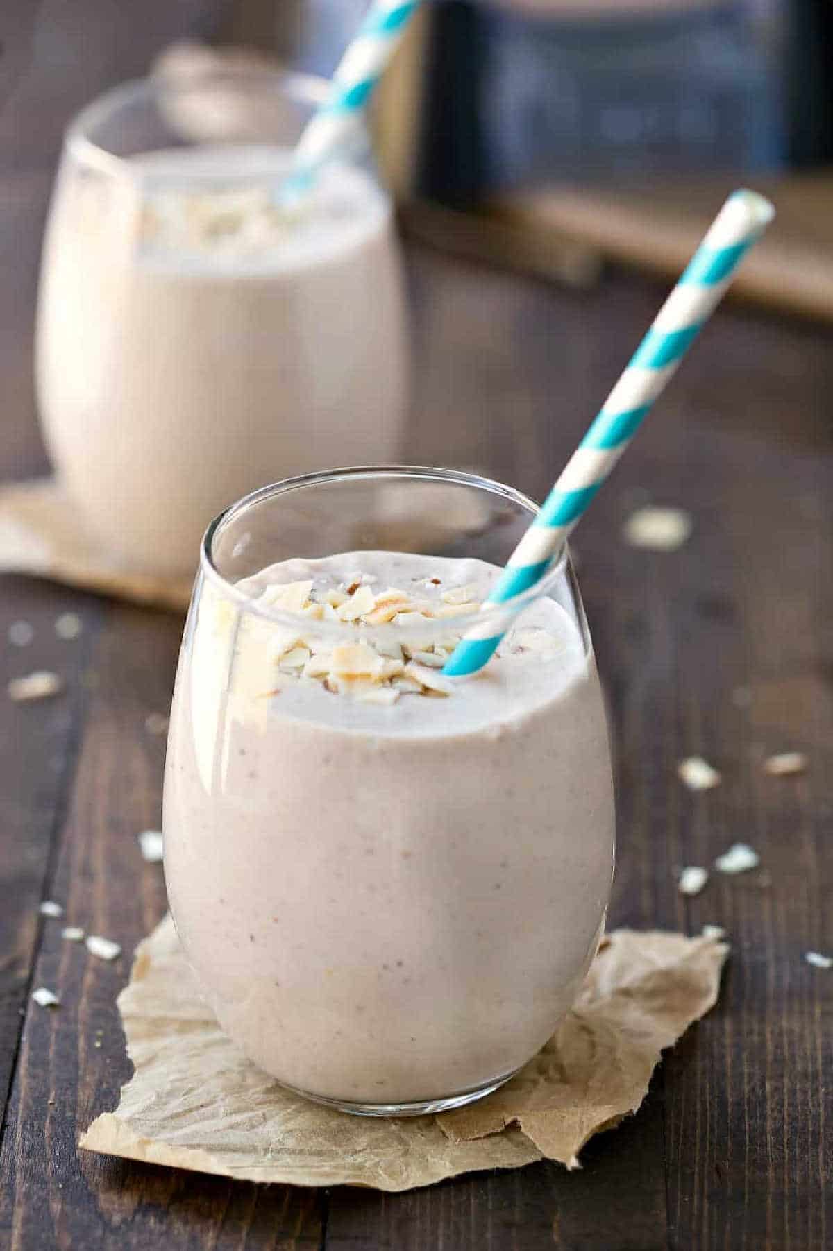 Two chocolate banana coconut almond smoothies with blue straws in them.