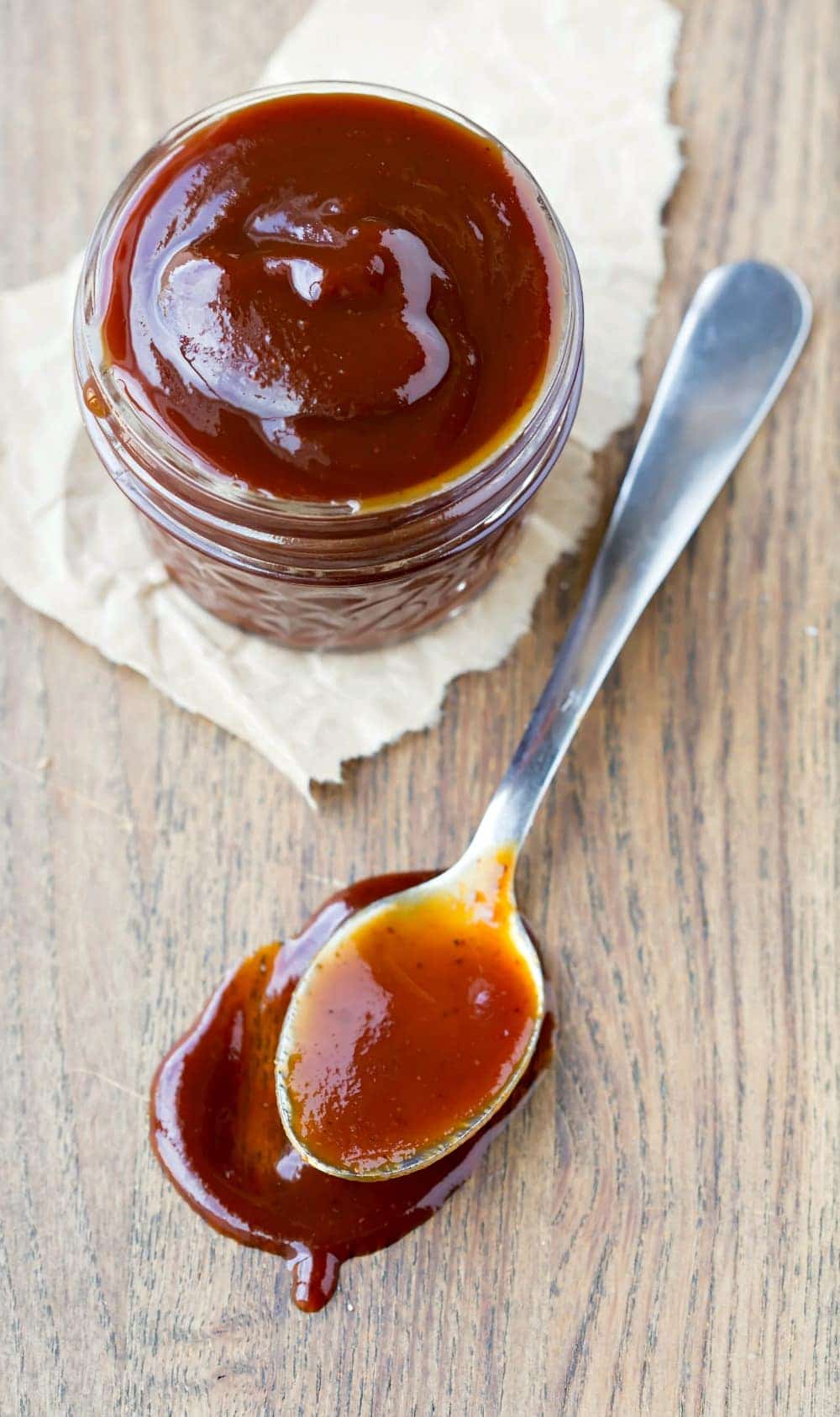 Homemade Kansas City Style Barbecue Sauce on a spoon next to a glass jar of bbq sauce