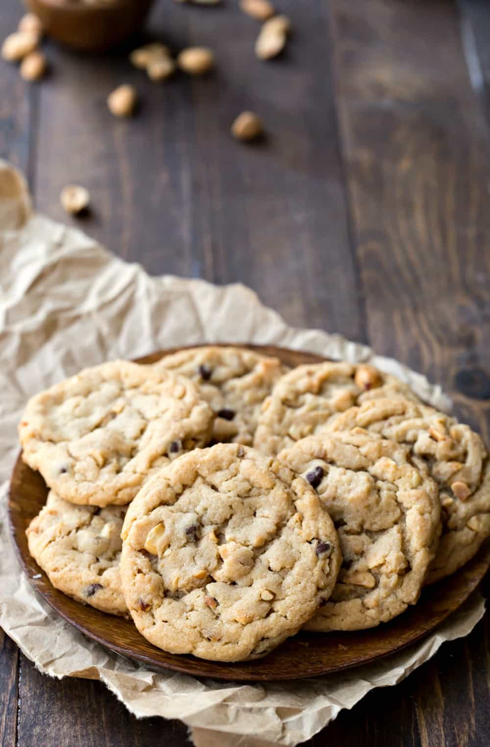 Peanut Butter Chocolate Chip Cookies on a wooden plate next to scattered peanuts