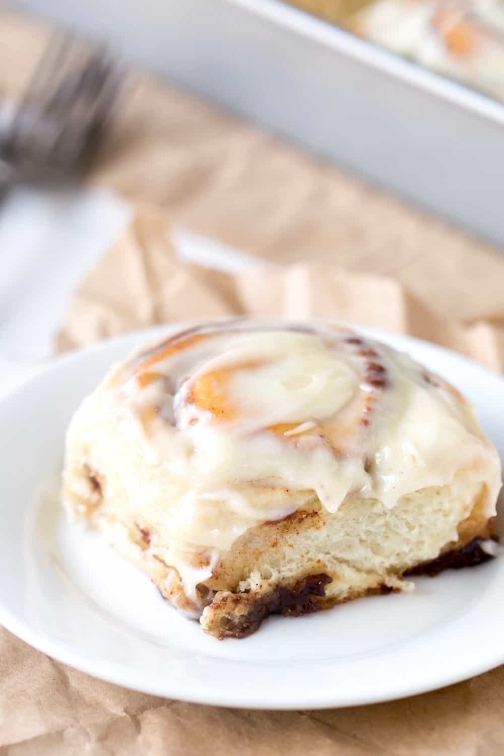Cinnamon Roll on a white plate on a piece of brown parchment paper