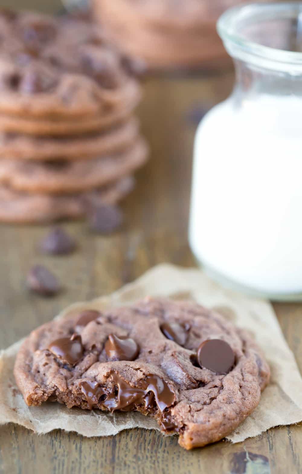 Chocolate Chocolate Chip Pudding Cookies on a piece of brown parchment paper next to a glass of milk