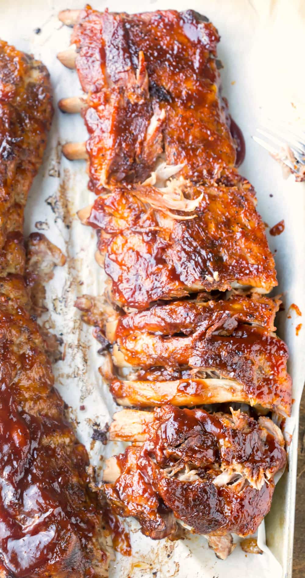 Slow cooker ribs coated in bbq sauce on a piece of parchment paper. 