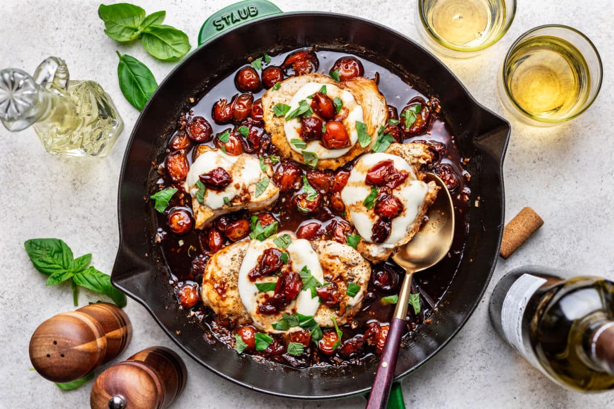 Caprese chicken in a skillet next to bottles of oil and vinegar. 
