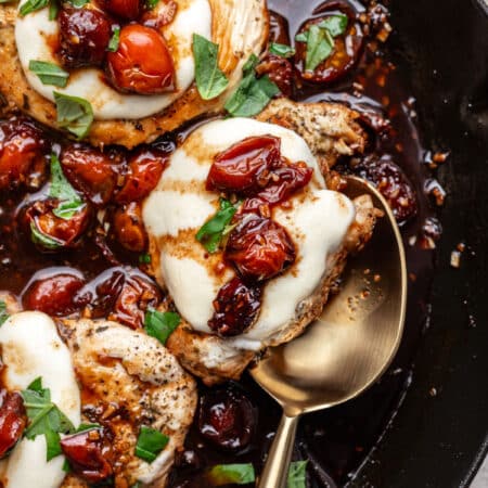A golden spoon partially underneath a piece of caprese chicken.
