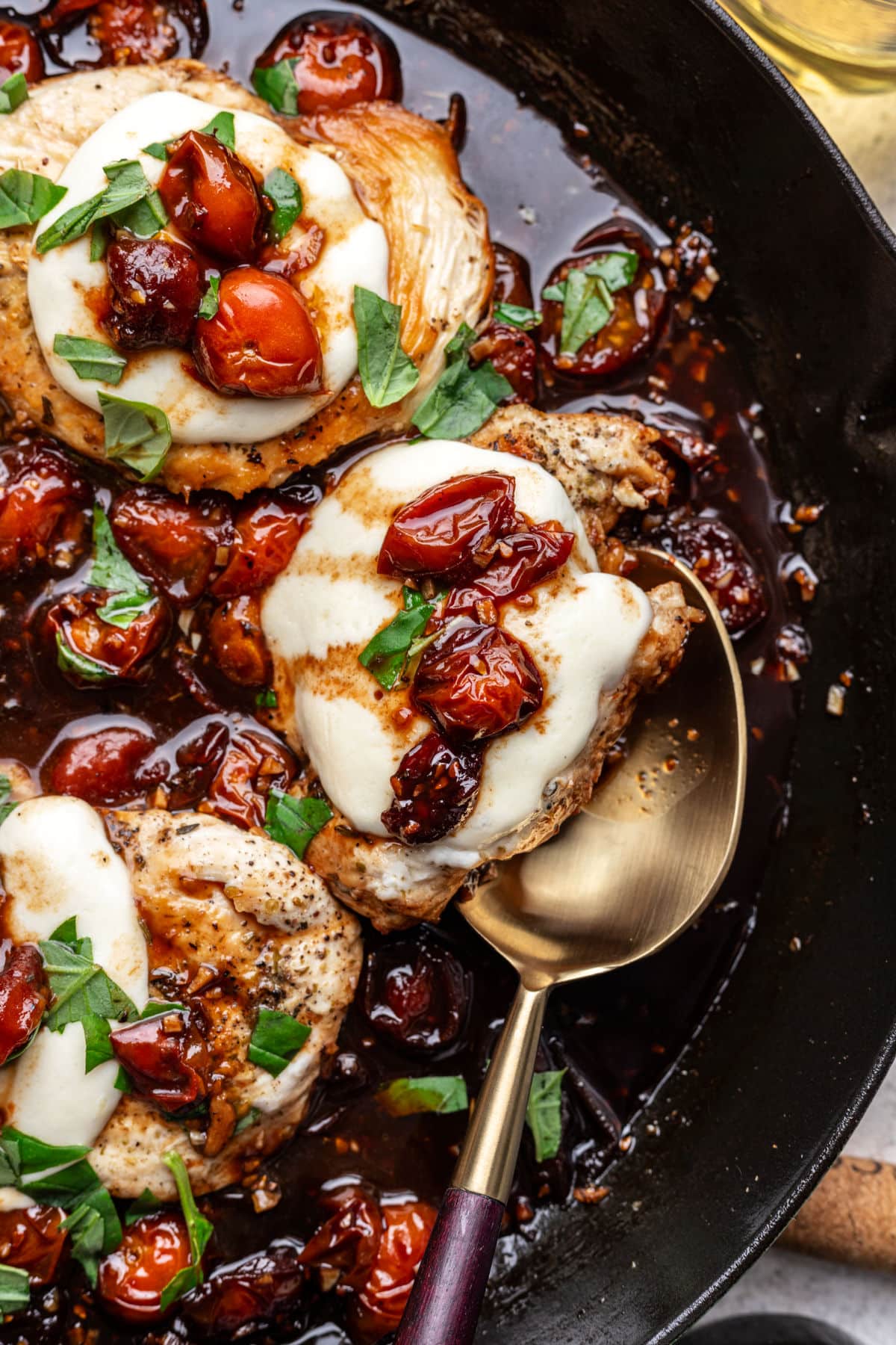 A golden spoon partially underneath a piece of caprese chicken.