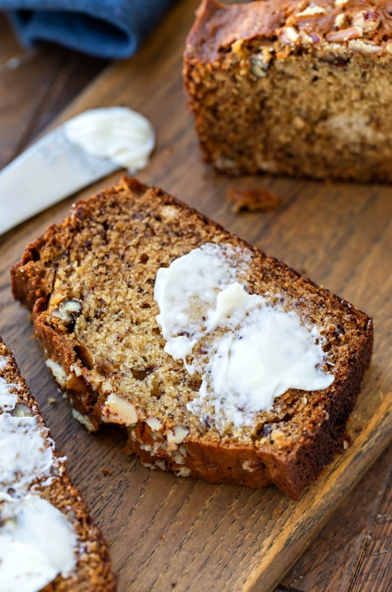 Slice of buttered banana nut bread on a wooden cutting board