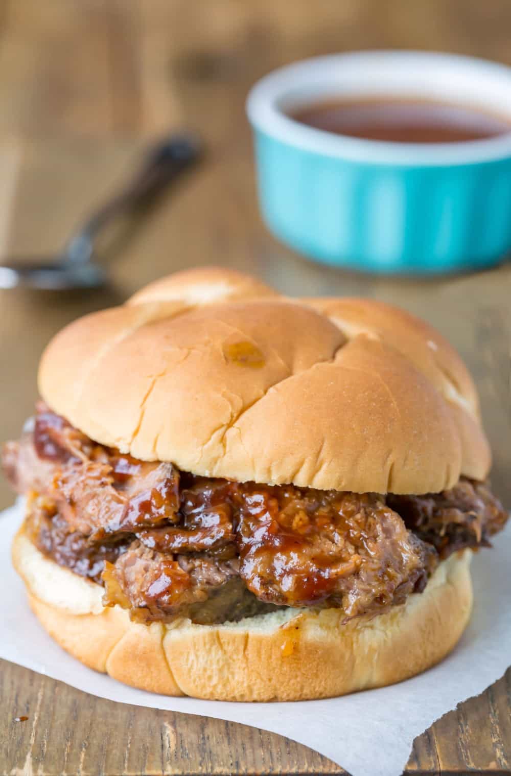Slow Cooker Texas Brisket on a sandwich bun next to a bowl of barbecue sauce