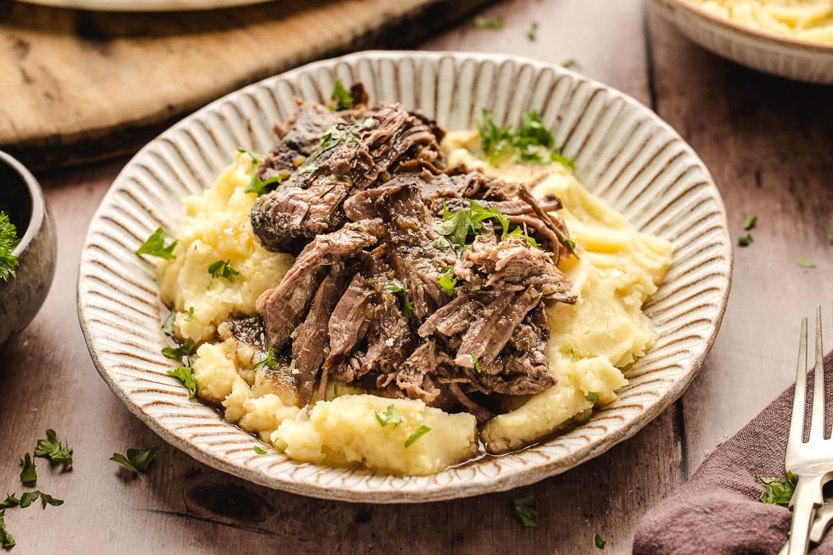 A plate of Mississippi pot roast over mashed potatoes topped with parsley.
