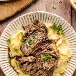 A dish of shredded Mississippi pot roast over mashed potatoes next to a dish of mashed potatoes.