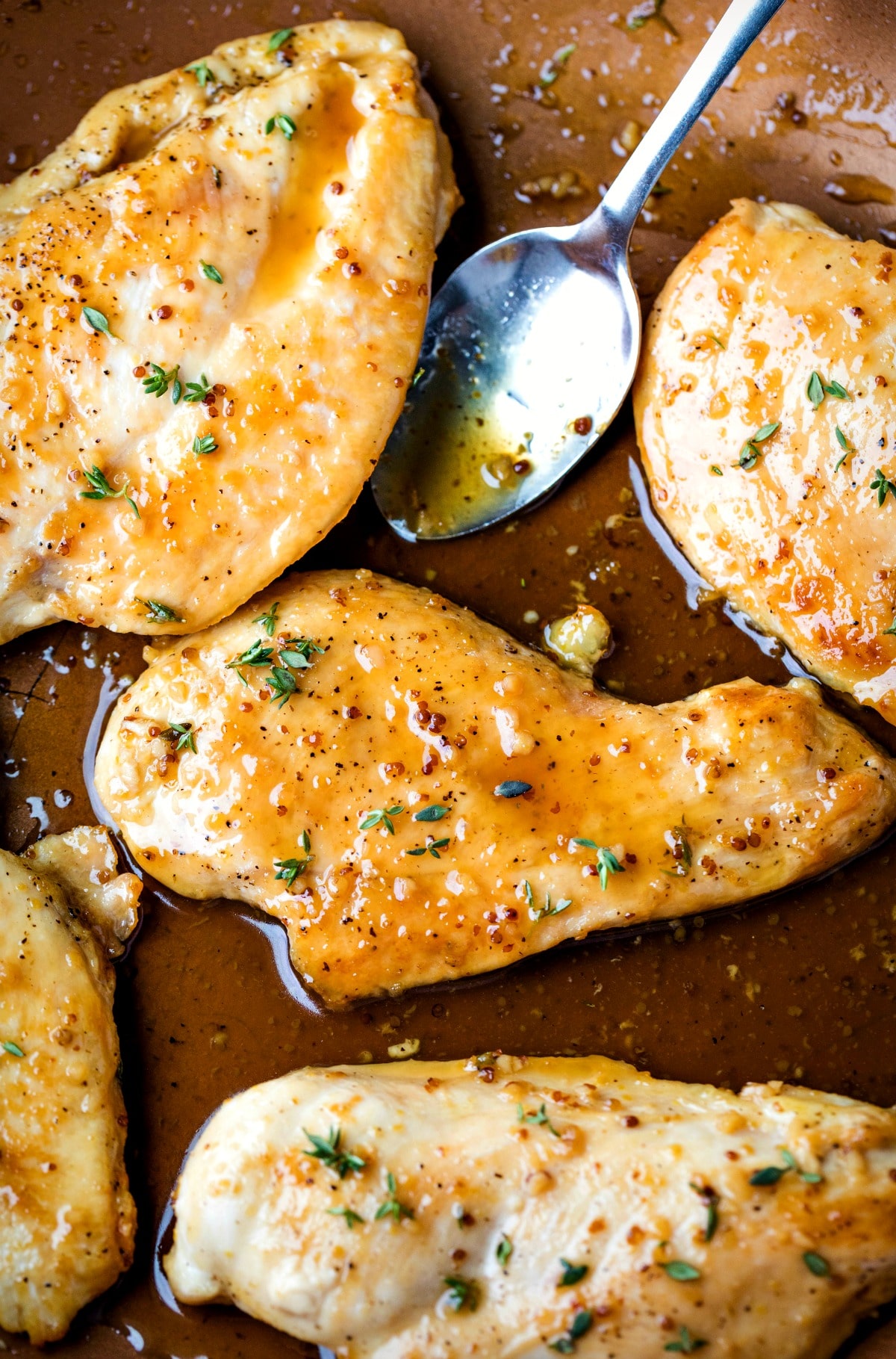 Silver spoon with sauce next to maple mustard glazed chicken in a pan