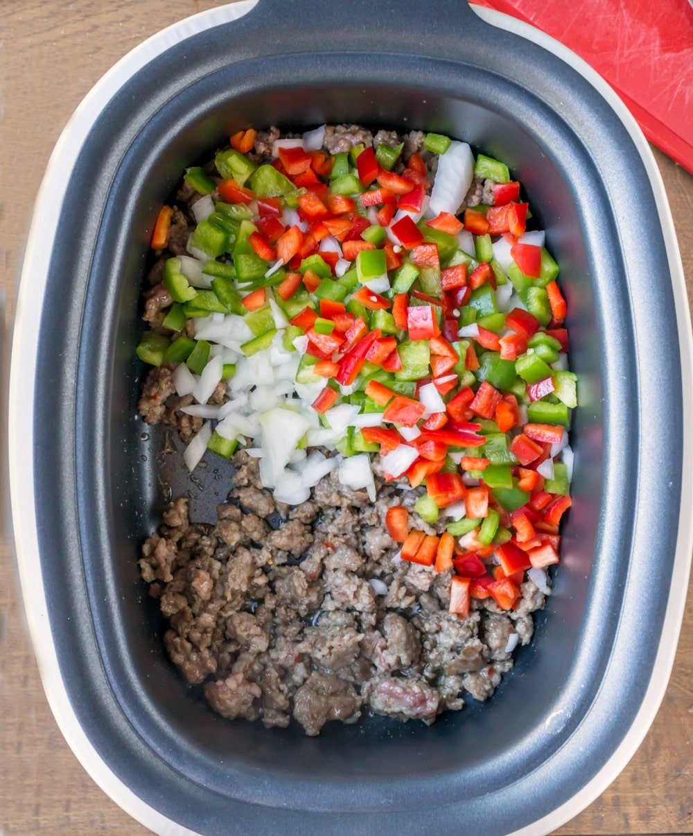 Onions peppers and browned Italian sausage in a slow cooker insert. 