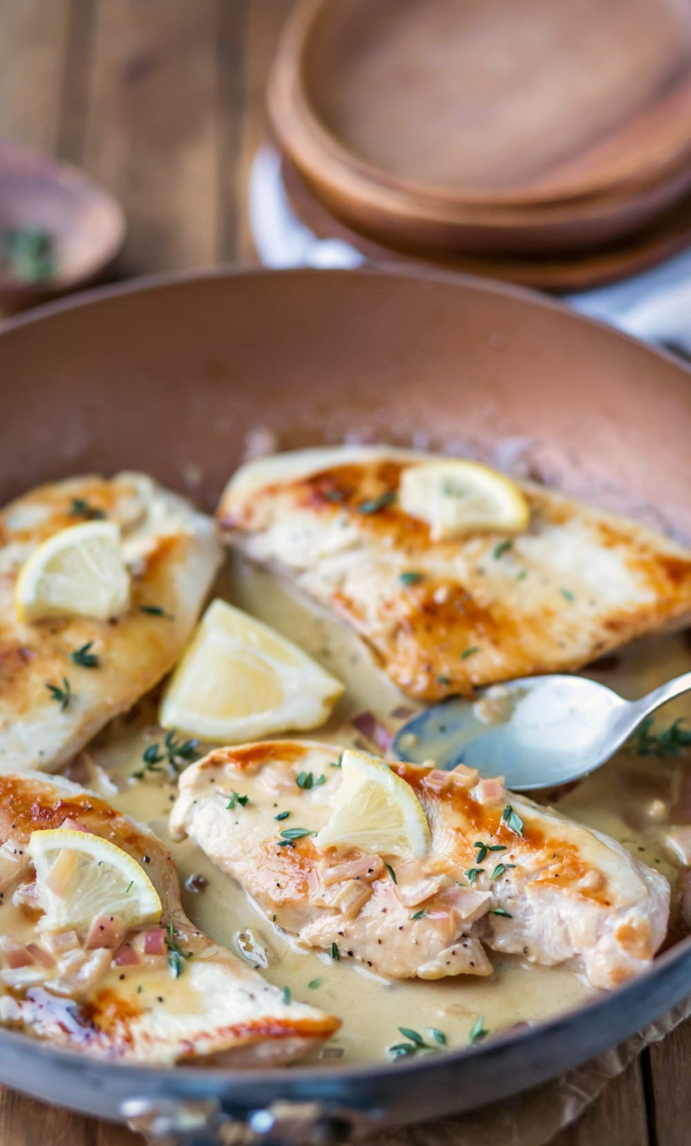 Lemon Garlic Chicken next to a silver spoon and a lemon wedge in a skillet