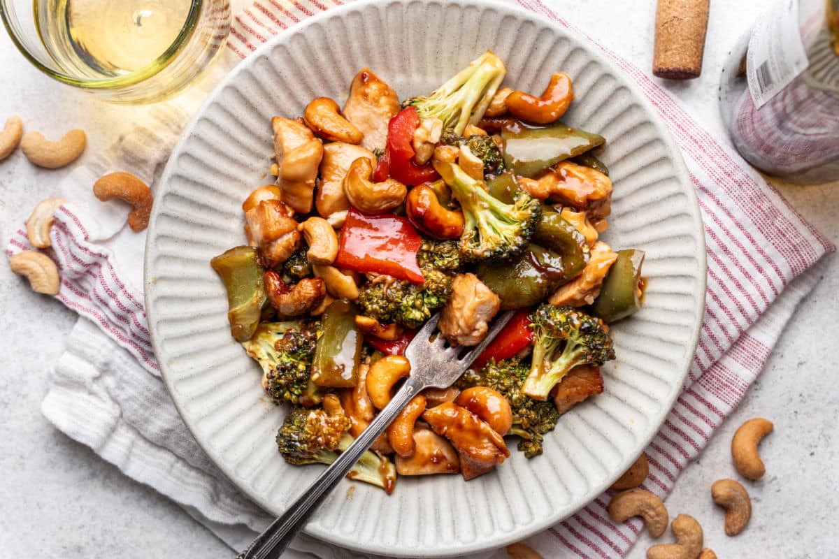 A plate of sheet pan cashew chicken with a fork in it.