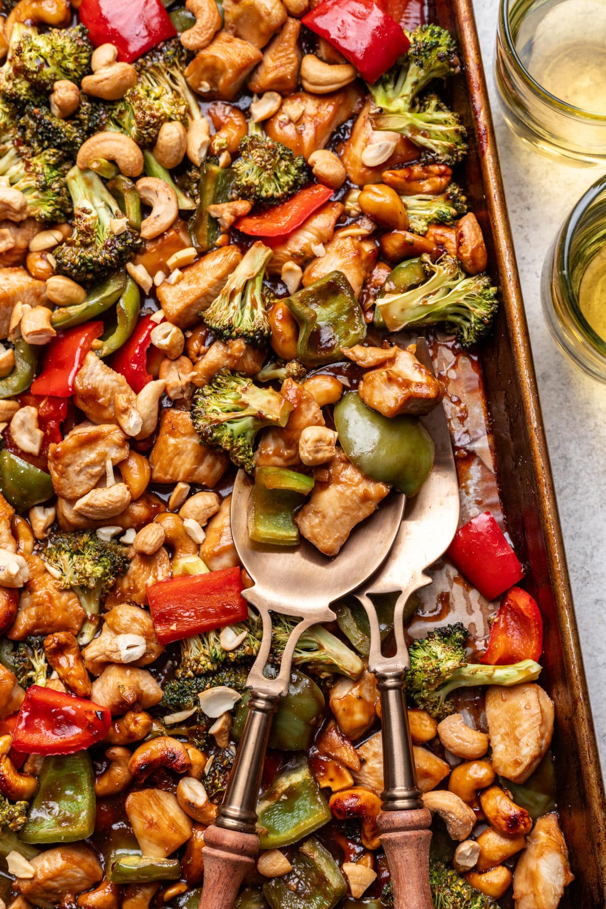 Two wooden handled spoons in a tray of sheet pan cashew chicken.