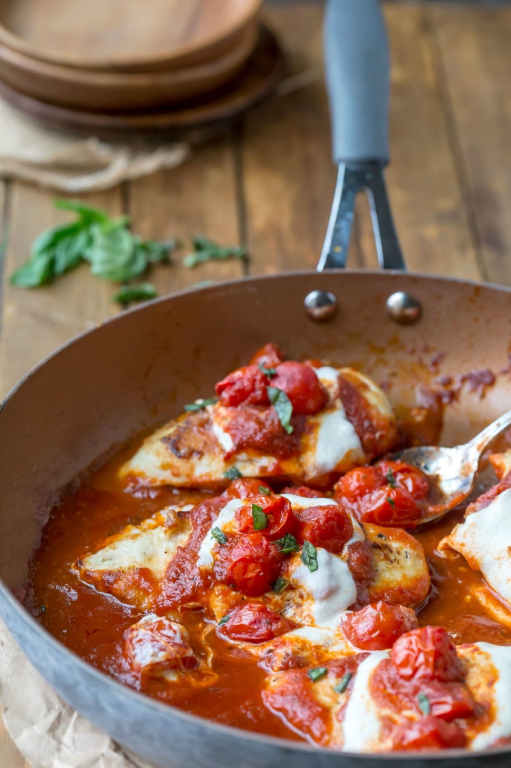 Skillet chicken parmesan in the pan with basil and plates behind it