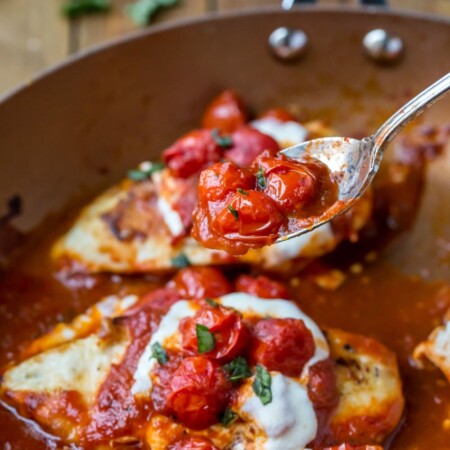 A spoon lifting sauteed tomatoes over skillet chicken parmesan.