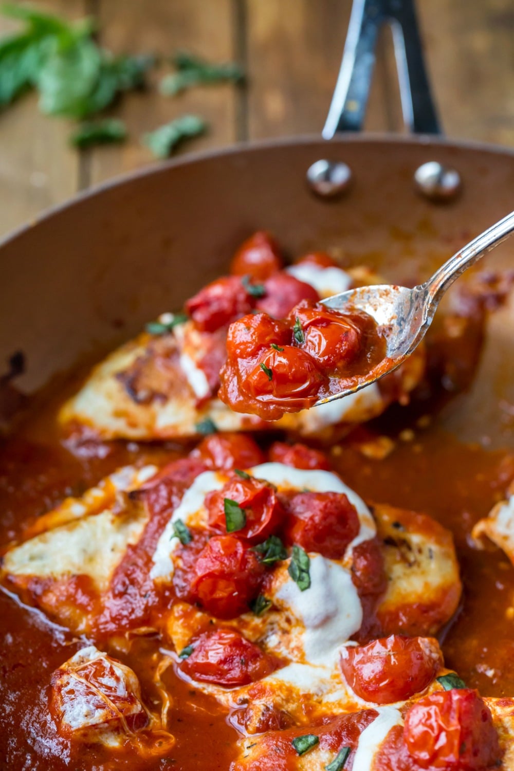 Spoon with tomato sauce above the skillet chicken parmesan