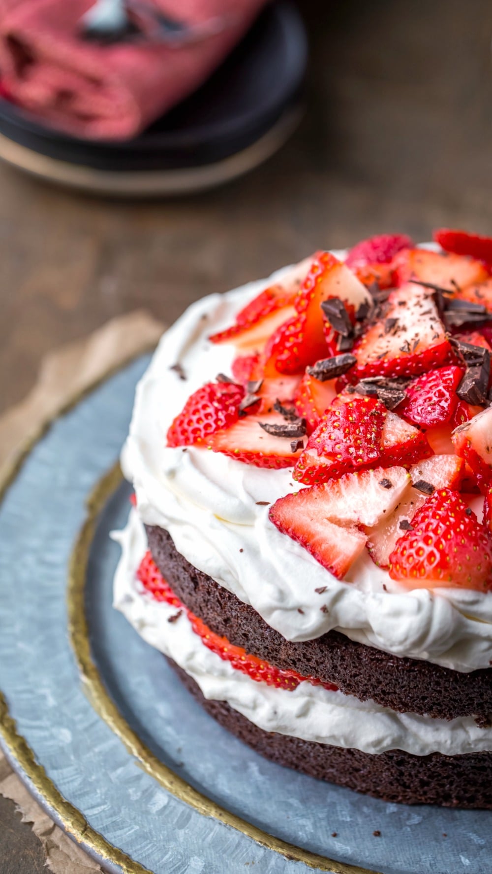 Strawberries and cream chocolate cake on a platter with plates and silverware in the background