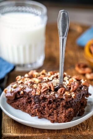 Slice of coca cola cake on a white plate with a silver fork in it.
