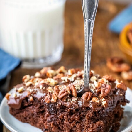 Slice of coca cola cake on a white plate with a silver fork in it.