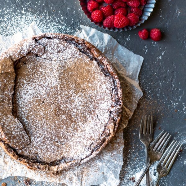Flourless chocolate cake on a board next to a bowl of raspberries