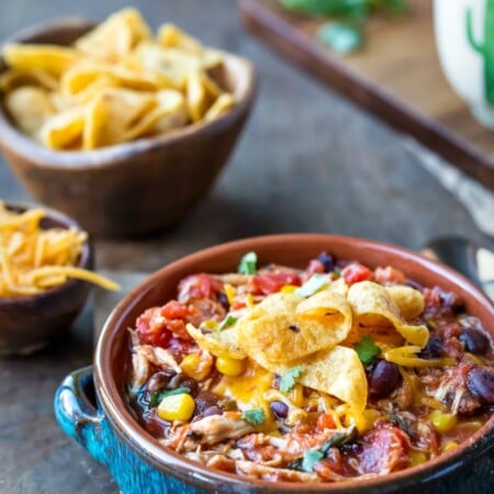 A dish of chicken frito chili next to dishes of fritos and shredded cheese.