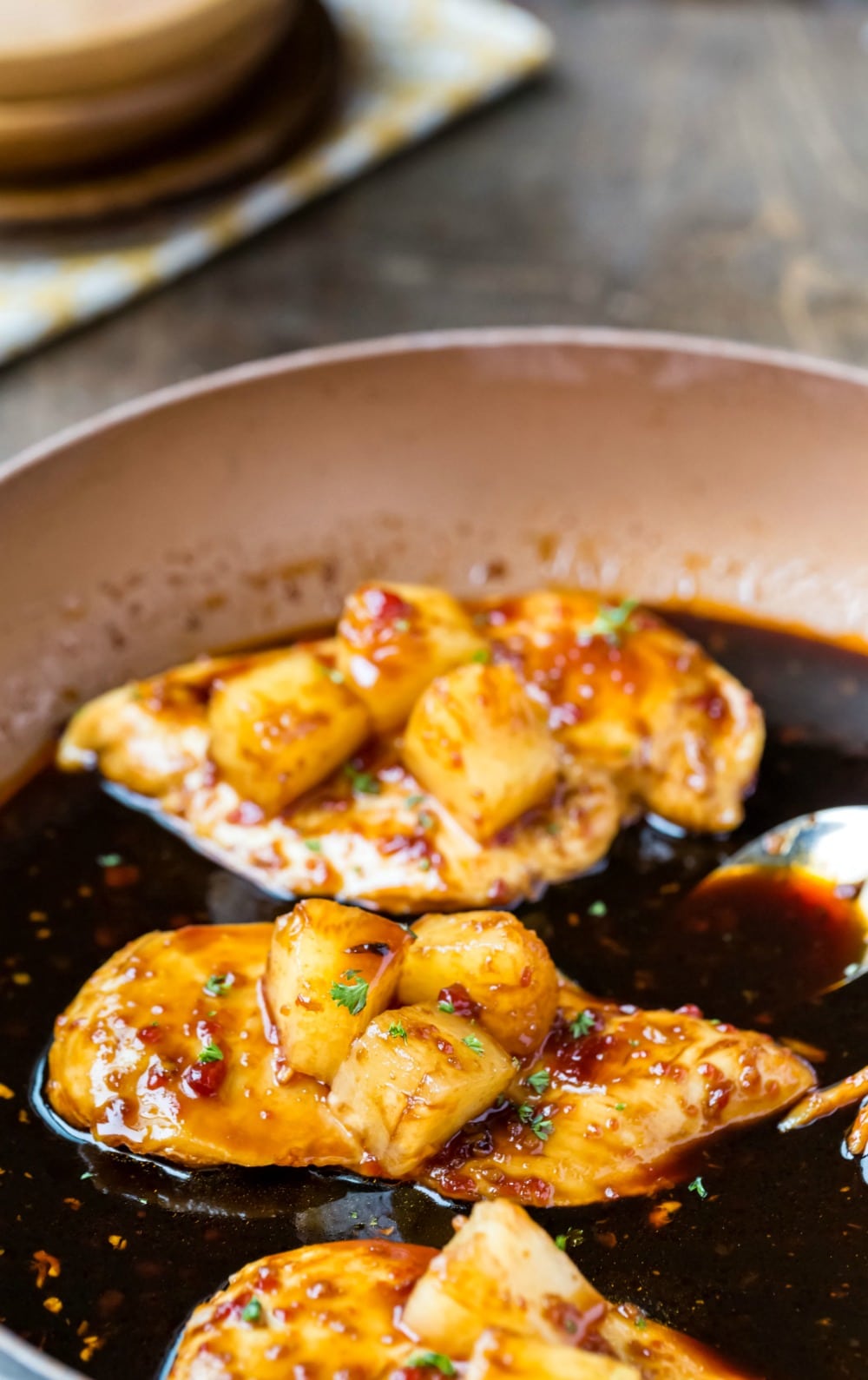 Pineapple chicken sitting in sauce and topped with pineapple in a skillet 