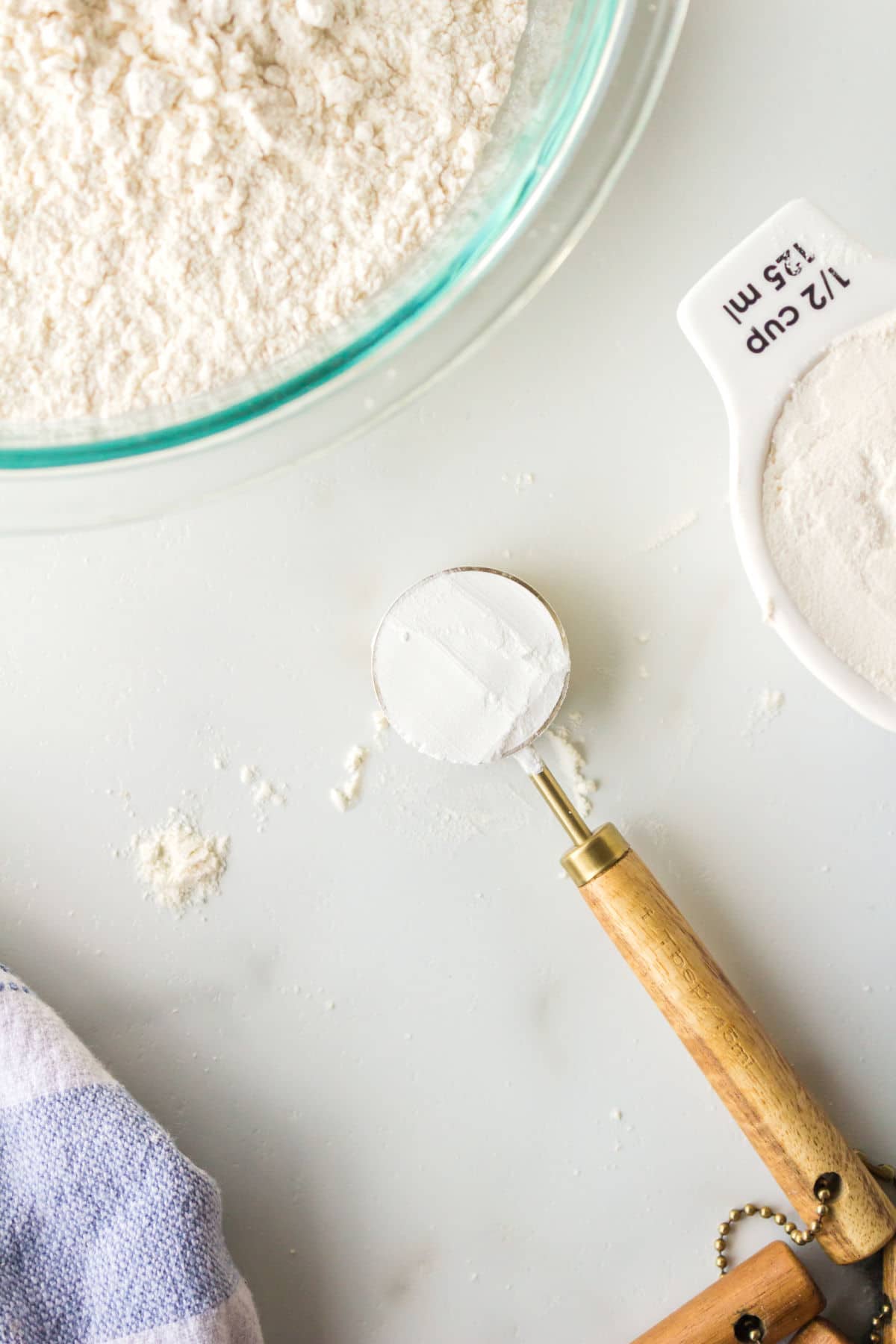 A measuring spoon with baking powder next to a bowl of flour.