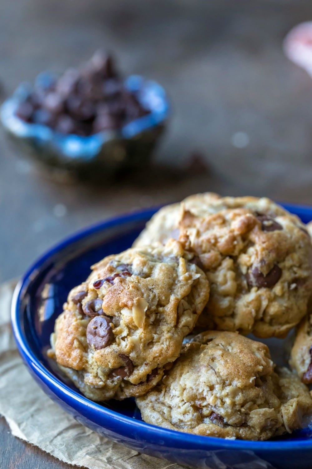 Easy chocolate chip oatmeal cookies on a blue plate next to a dish of chocolate chips