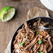 Mexican shredded beef in a metal dish next to sliced limes