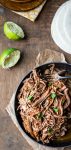 Mexican shredded beef in a metal dish next to sliced limes