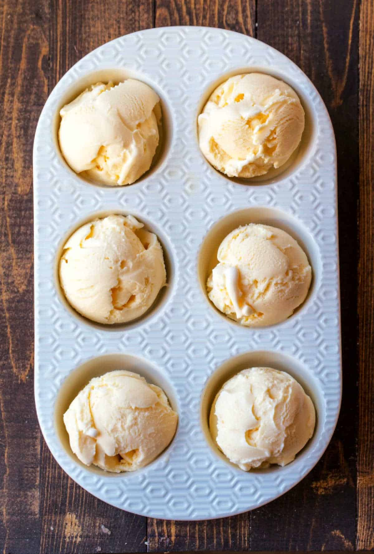 6 scoops of vanilla ice cream in a muffin tin.