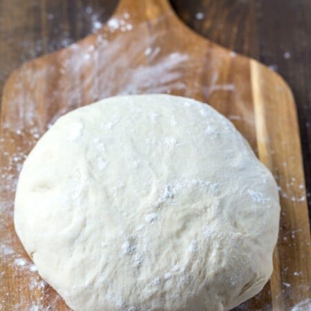 Ball of pizza dough on a wooden cutting board