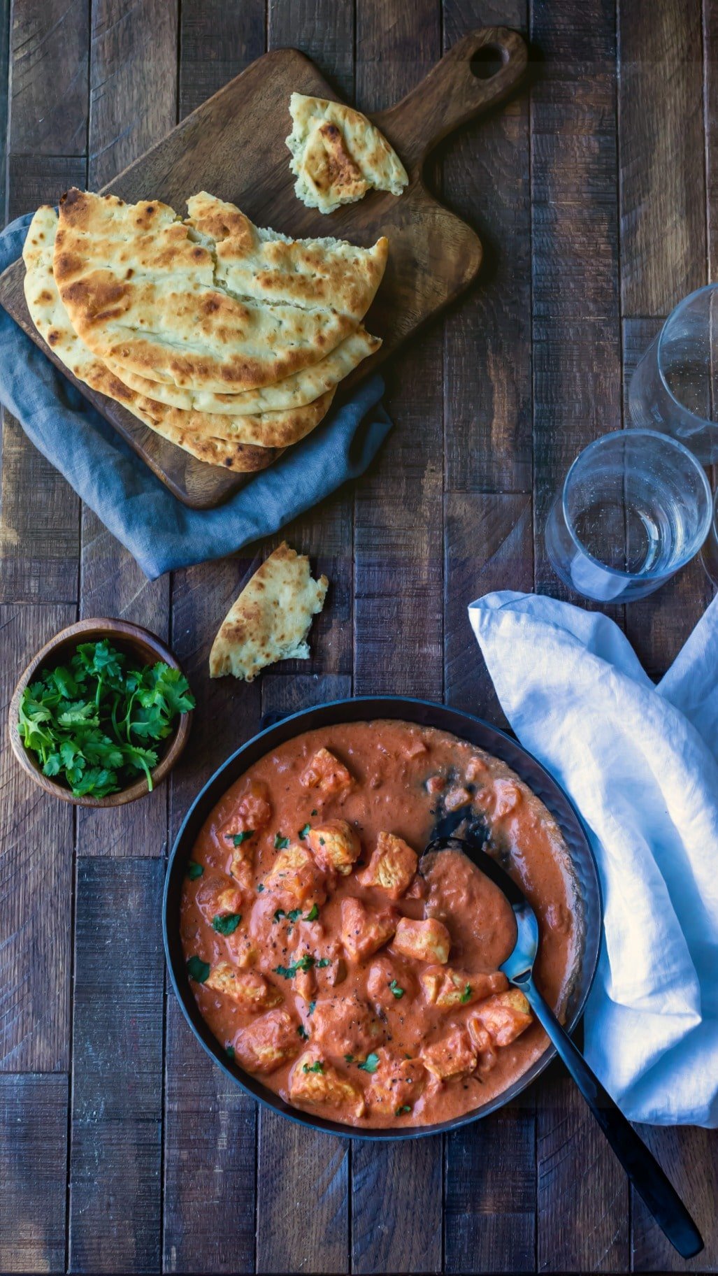 Dish of easy chicken tikka masala next to a bowl of cilantro and pieces of naan