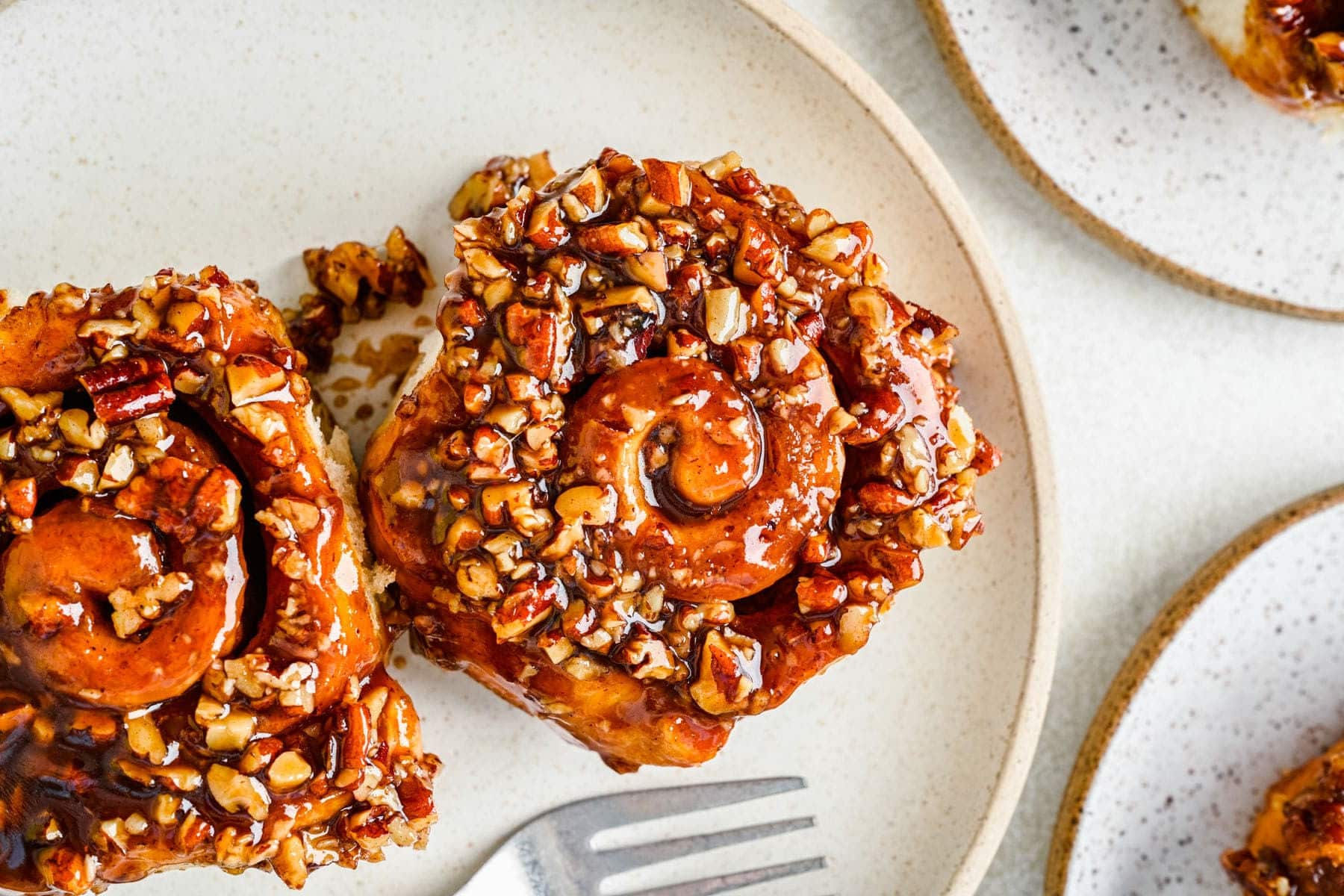 Two sticky buns on a cream plate next to a fork.