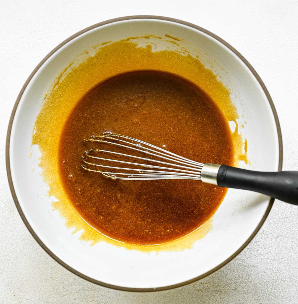Sticky bun topping in a white mixing bowl with a whisk in it.
