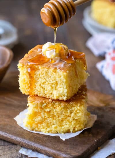 Two pieces of sweet cornbread stacked on top of each other with honey pouring onto the top piece.