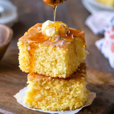 Two pieces of sweet cornbread stacked on top of each other with honey pouring onto the top piece.