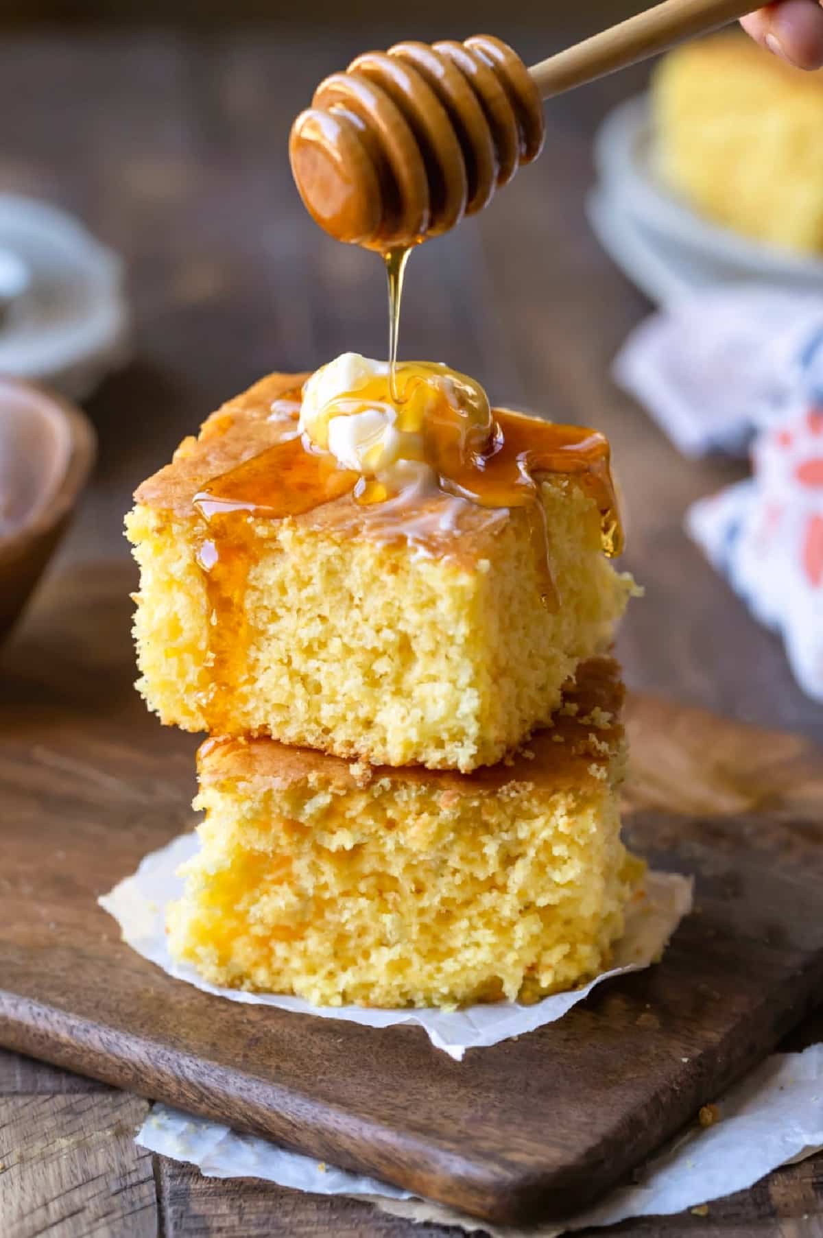Two pieces of sweet cornbread stacked on top of each other with honey pouring onto the top piece.