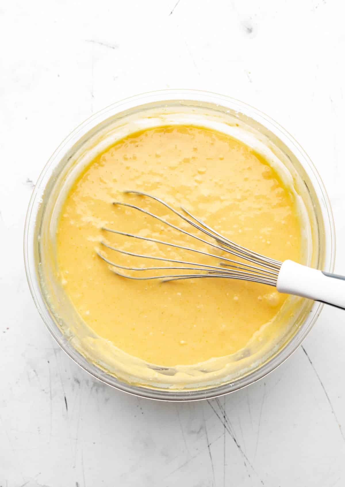 Sweet cornbread batter in a glass mixing bowl with a whisk in it.