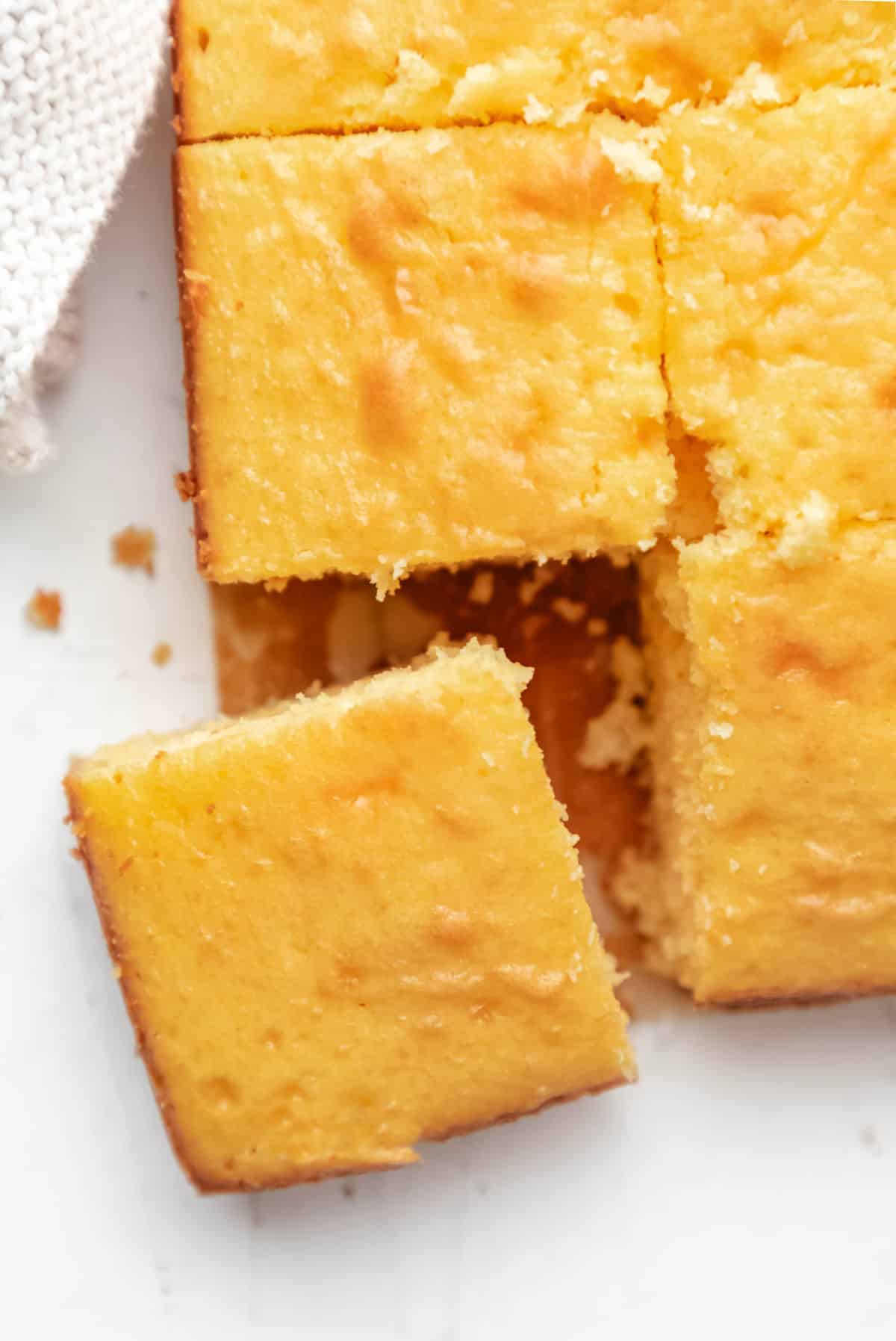 A cut piece of cornbread at an angle next to the pan of cornbread.