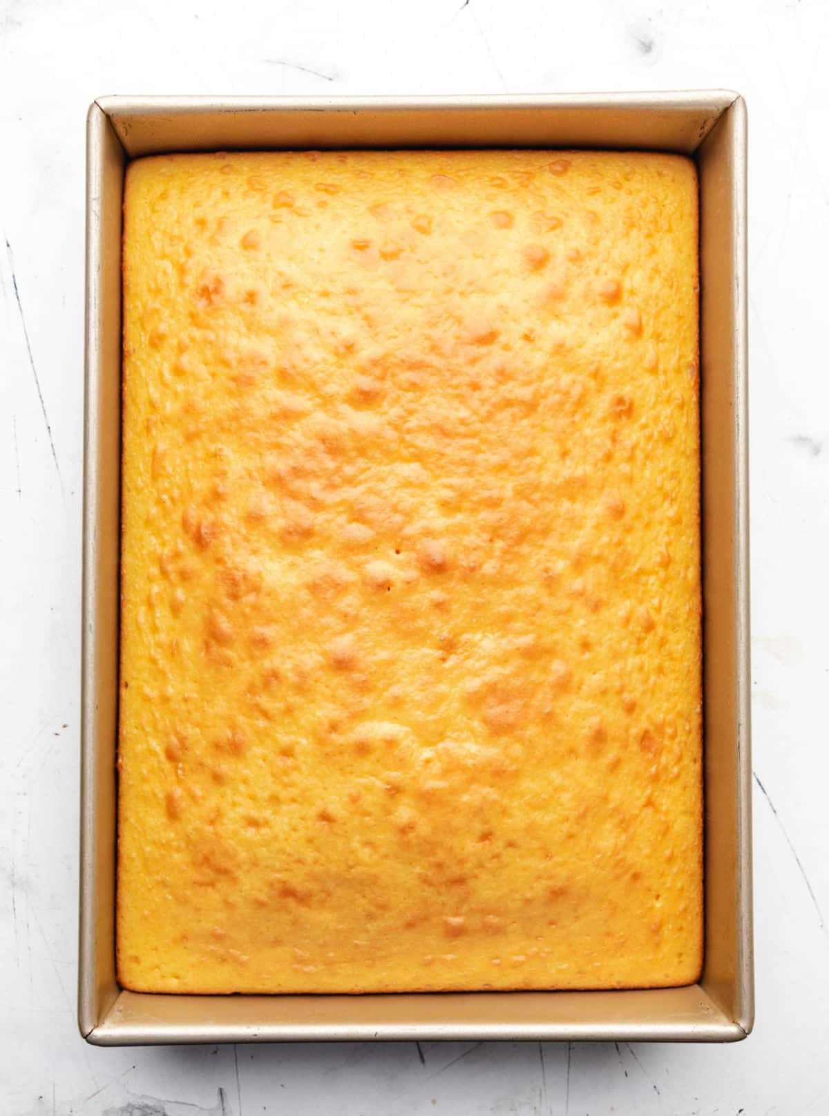 Pan of baked cornbread with cake mix on a marble background.