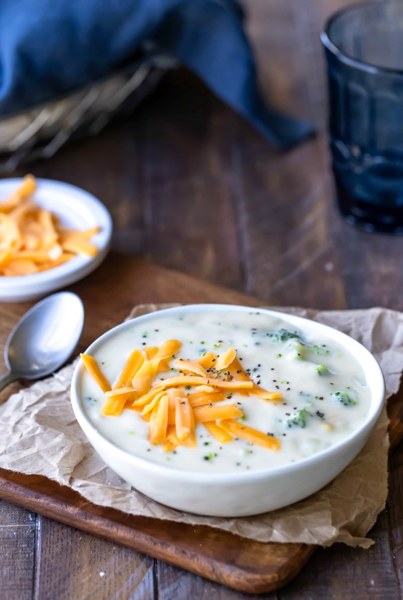 Broccoli Cheeese Soup topped with cheddar cheese in a white bowl next to a silver spoon