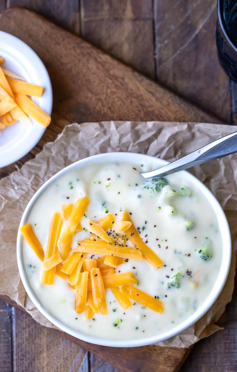 Dish of broccoli cheese soup on a piece of brown parchment paper next to a dish of cheese