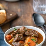 Beef stew in a white bowl next to two black spoons
