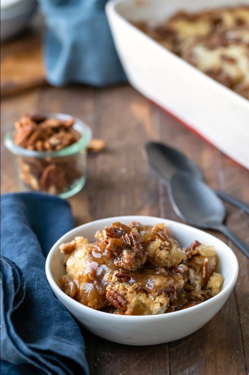 Pecan pie pudding cake in a white dish next to a blue linen napkin and two black spoons