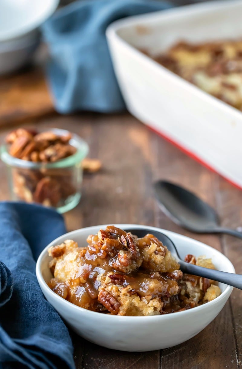 Pecan pie pudding cake in a white dish next to a glass jar with pecans